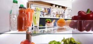 Portrait of female standing near open fridge full of healthy food, vegetables and fruits. Portrait of female