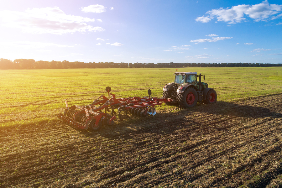Agricultural tractor plowing the field at sunset. Agricultural machinery in field