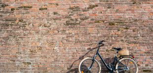 Black retro vintage bicycle with old brick wall and copy space. Retro bicycle with basket in front of the old brick wall. Retro bicycle on roadside with vintage brick wall background.