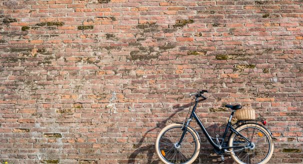 Black retro vintage bicycle with old brick wall and copy space. Retro bicycle with basket in front of the old brick wall. Retro bicycle on roadside with vintage brick wall background.