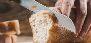 Whole grain bread put on kitchen wood plate with a chef holding gold knife for cut. Fresh bread on table close-up. Fresh bread on the kitchen table The healthy eating and traditional bakery concept. Rustic style