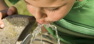 A picture of a little boy drinking from a water fountain.