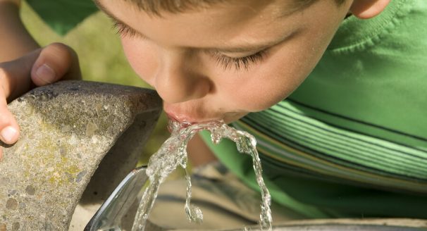 A picture of a little boy drinking from a water fountain.