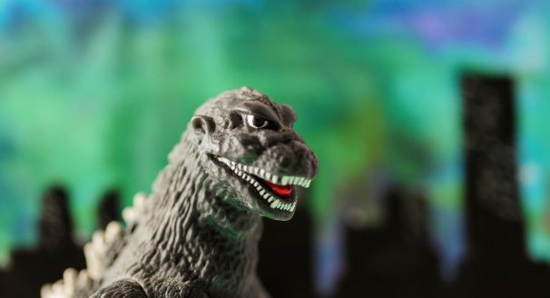 A Godzilla toy stands before a backround depicting a city.