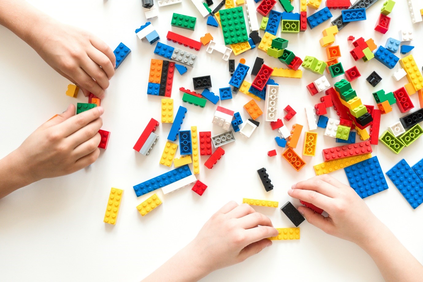 Four hands playing with lego bricks.