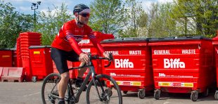 A cyclist on the Ride for Freedom rides past a row of large Biffa bins.