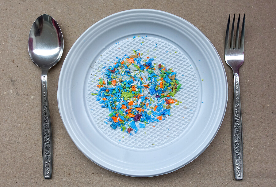 High angle view of microplastics on a single use plate with fork and spoon on top. Creative concept of water pollution and global warming. 