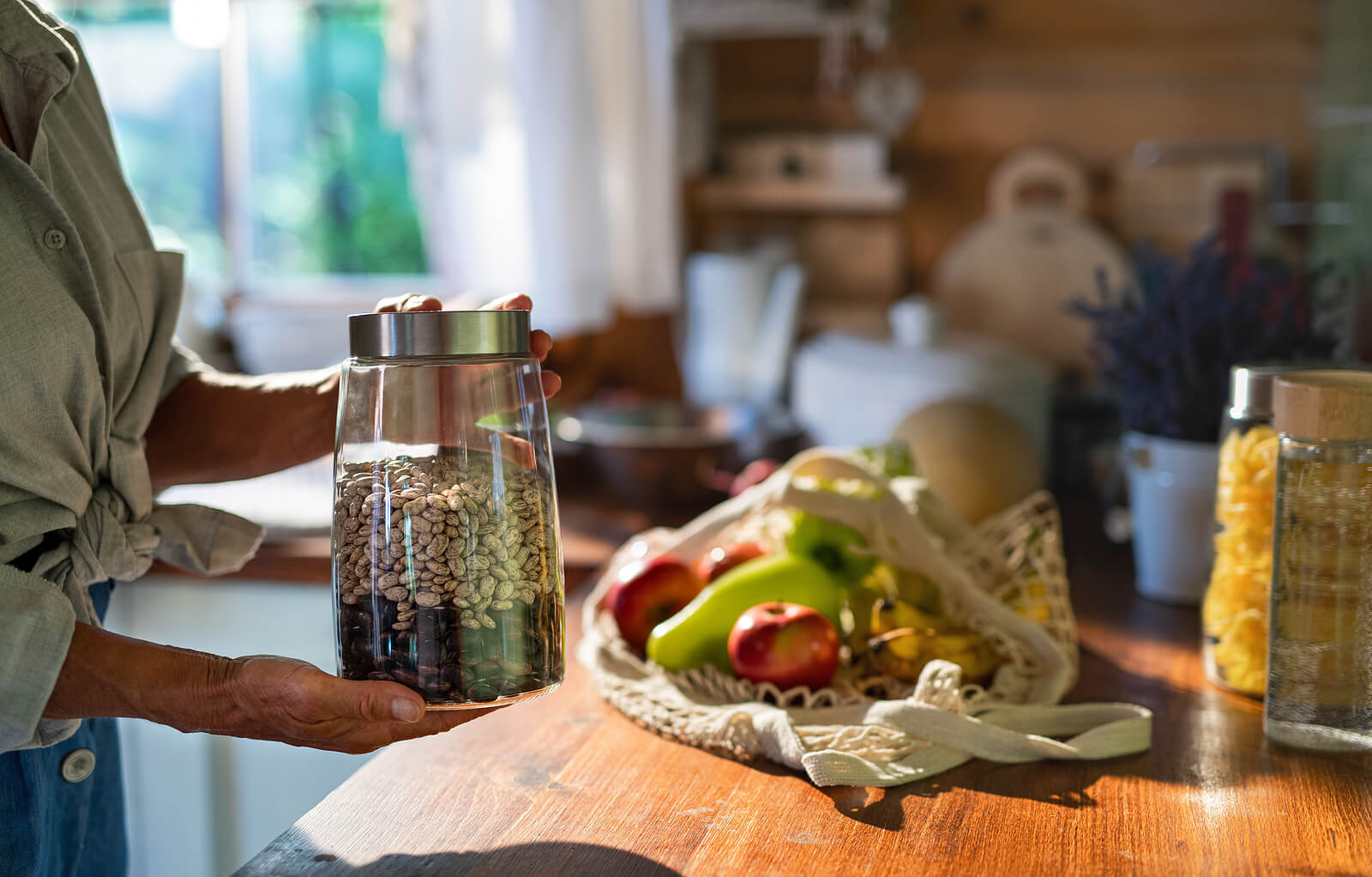 Close-up of senior woman unpacking local food in zero waste packaging from bag in kitchen at home.