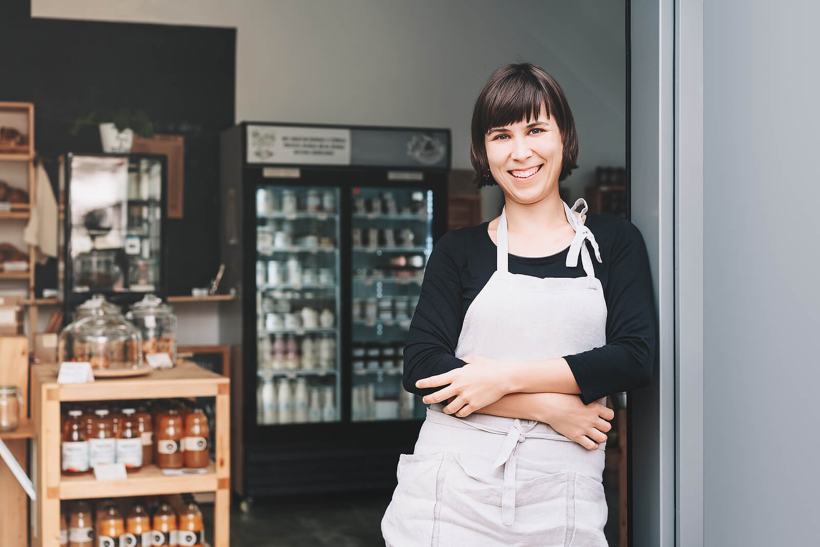 Portrait of owner of sustainable small local business. Shopkeeper of zero waste shop standing on interior background of shop. Smiling young woman in apron welcoming at entrance of plastic free store