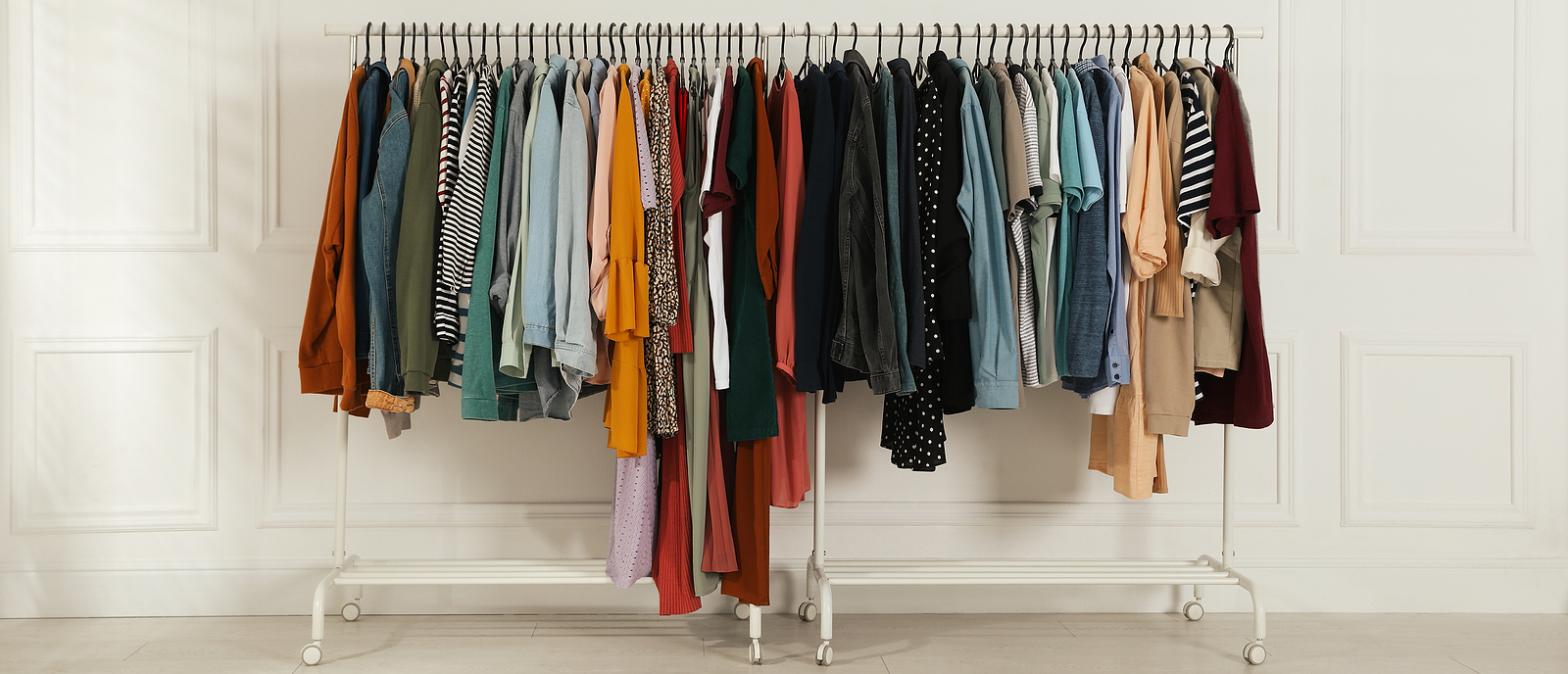 Racks with stylish clothes near white wall indoors, banner design. Fast fashion