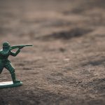 A green toy soldier poses to shoot his rifle.
