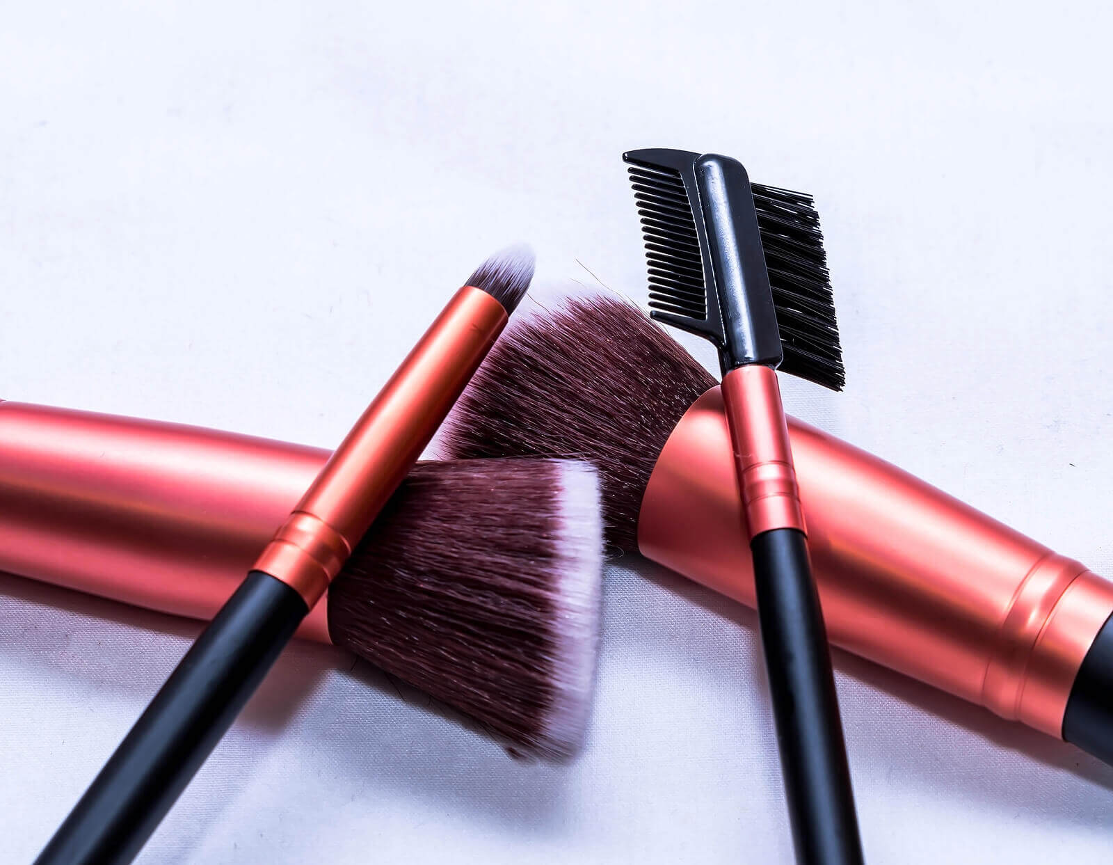 Four make up brushes sit across one another on a white table.