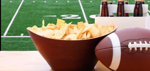 Chips, a six pack of beer, and an American football in front of the Super Bowl on TV.
